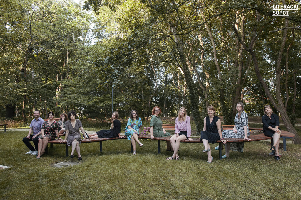 Zdjęcie przedsawia grupę osób siedzących na ławce w parku